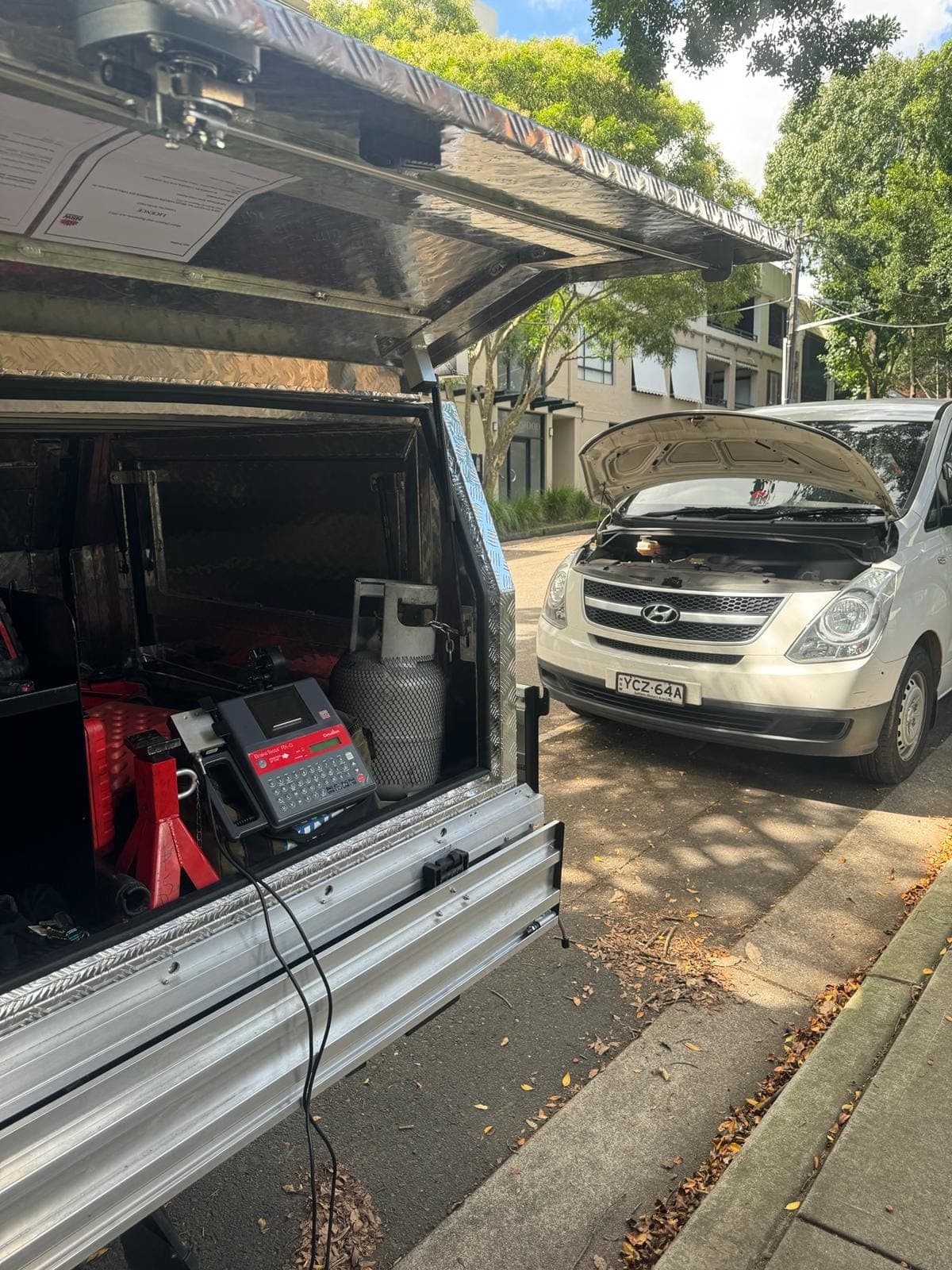 The test gear in a PSA ute’s open canopy, with a van behind it waiting with its bonnet up