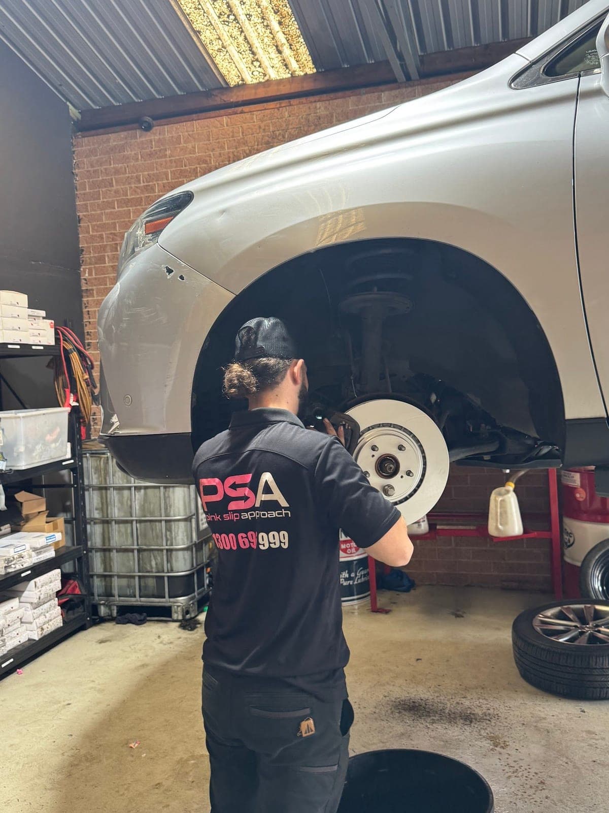 A PSA technician checking the front brake disc of a silver SUV raised on a hoist in the workshop