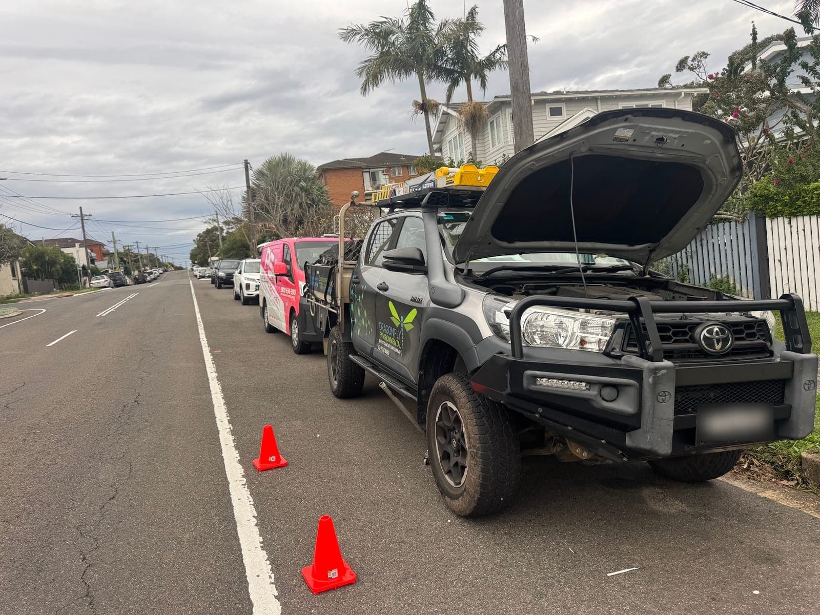 A business’s Toyota HiLux work ute with its bonnet up on a suburban street, cones set out and PSA vehicles parked behind