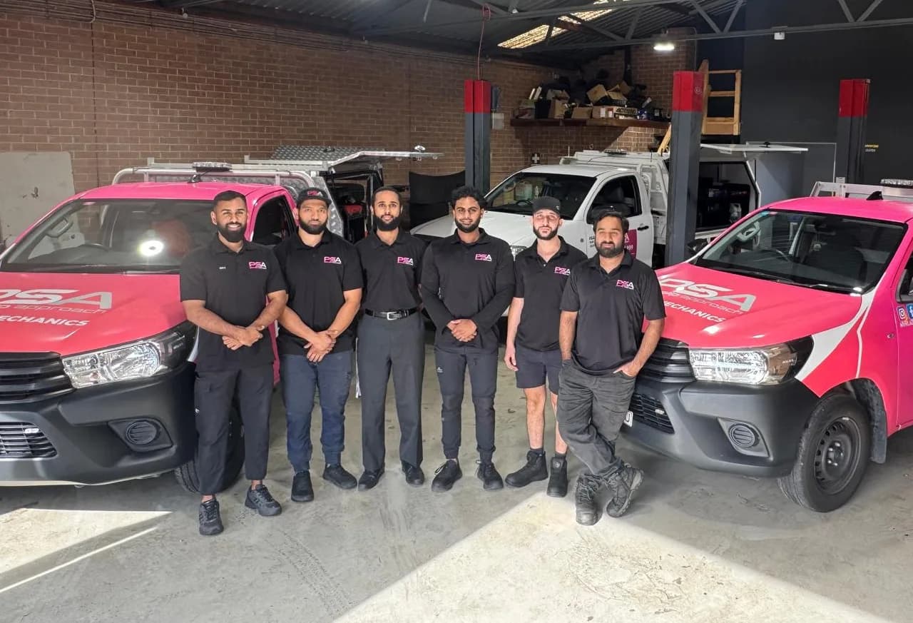 The Pink Slip Approach team standing between two pink service utes in their workshop
