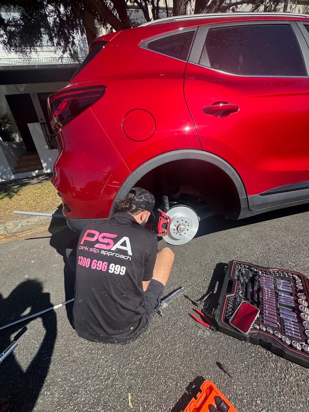 A PSA technician working beside the exposed rear brake disc of a red SUV
