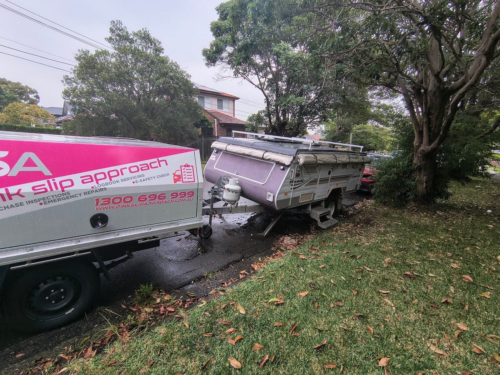 A pop-top camper trailer on a grass verge behind a PSA service ute, on a wet day