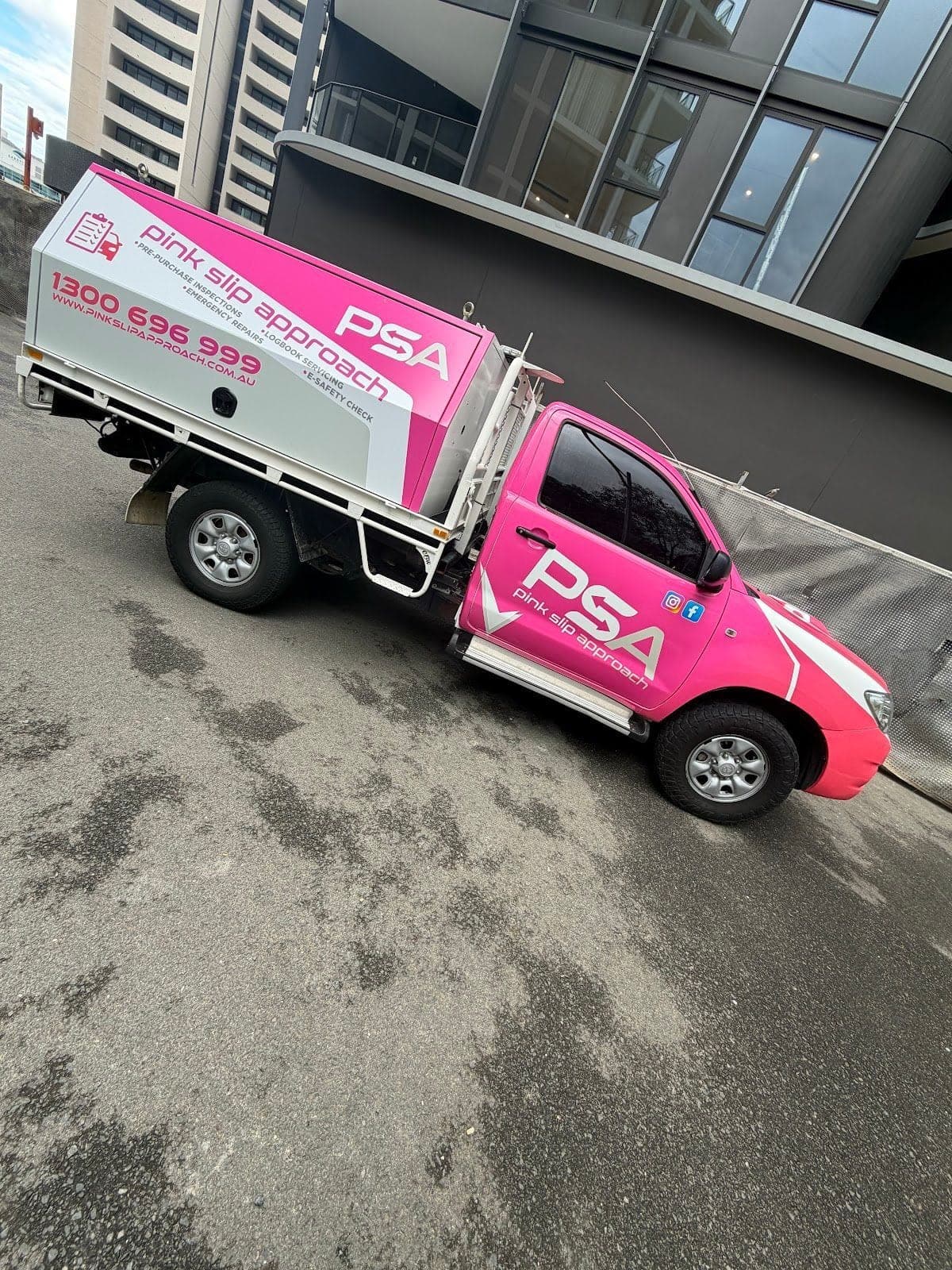 A pink PSA service ute parked on a sloping street beside apartment buildings