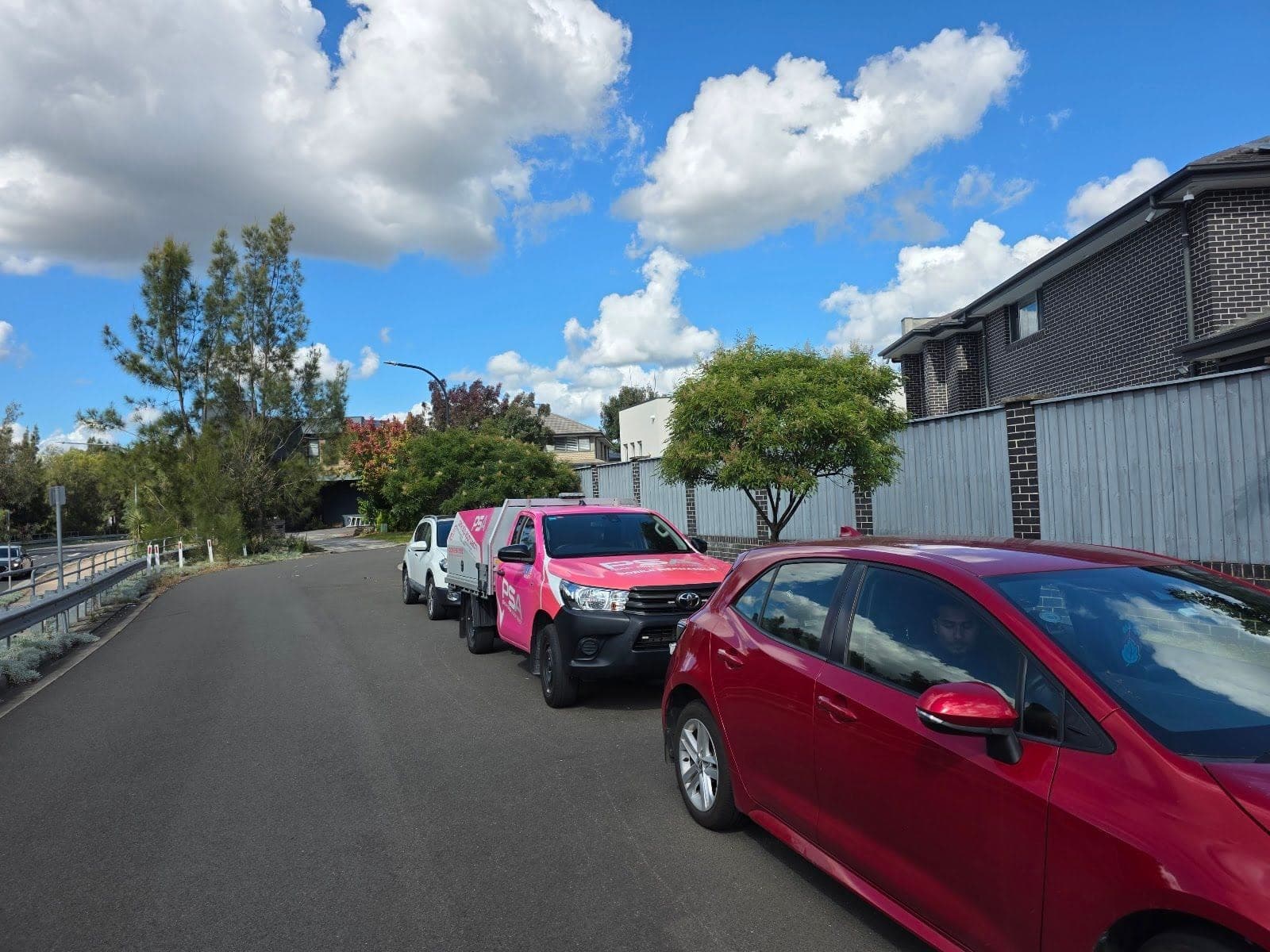 A red Toyota Corolla parked on a suburban street, a pink PSA ute behind it