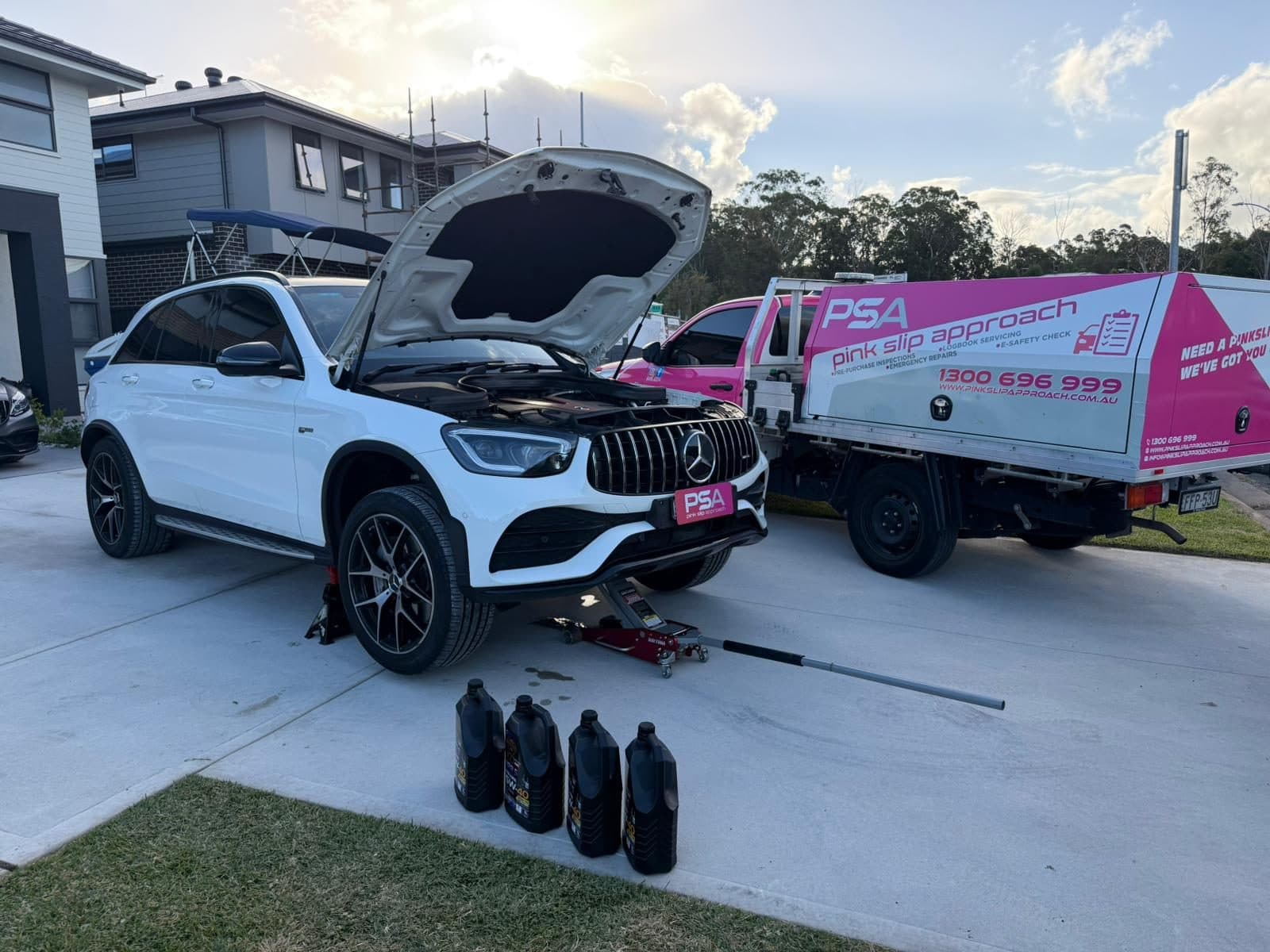 A Pink Slip Approach ute parked beside a white Mercedes with its bonnet up on a home driveway