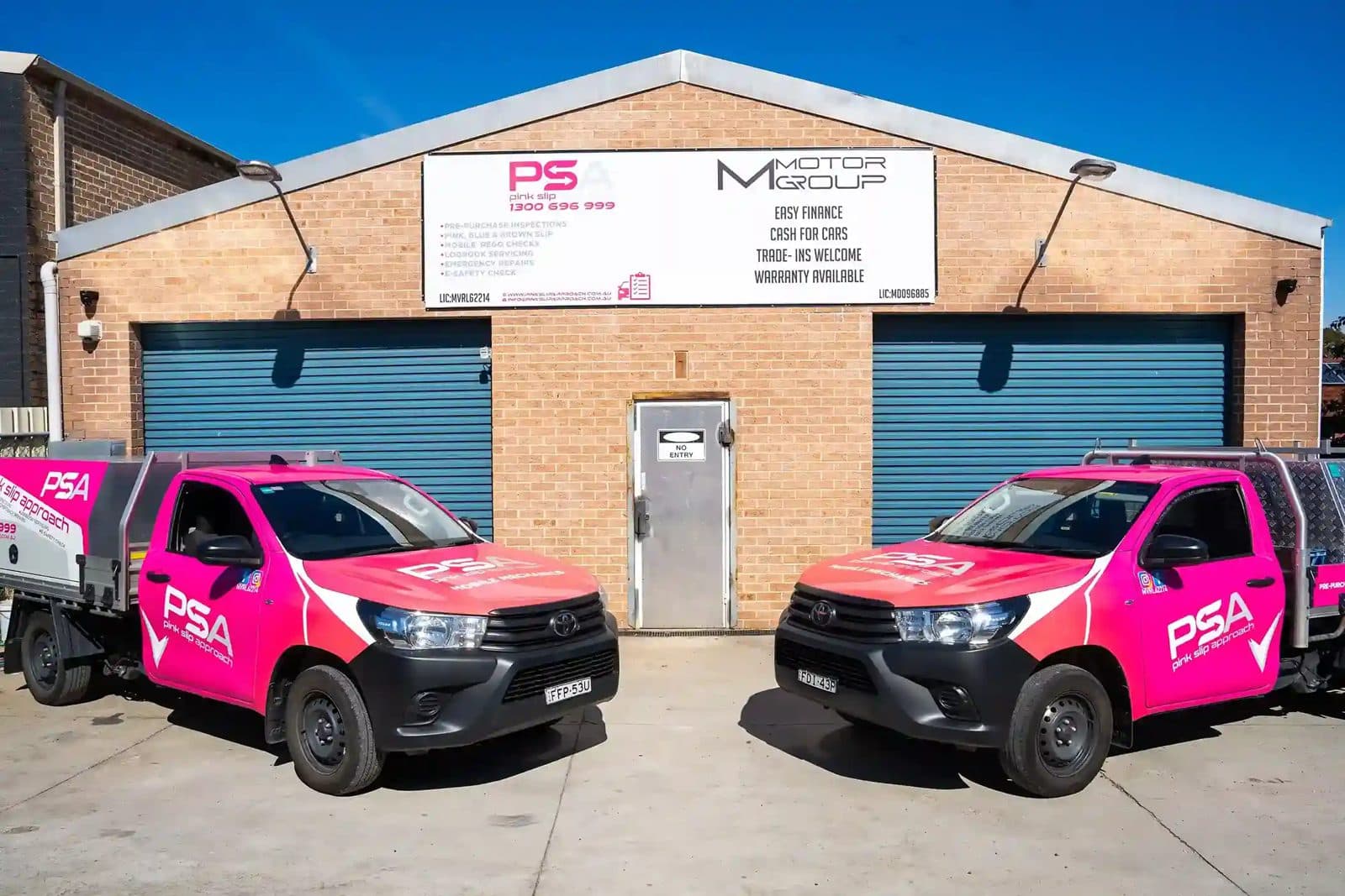 Two Pink Slip Approach utes parked outside a brick workshop