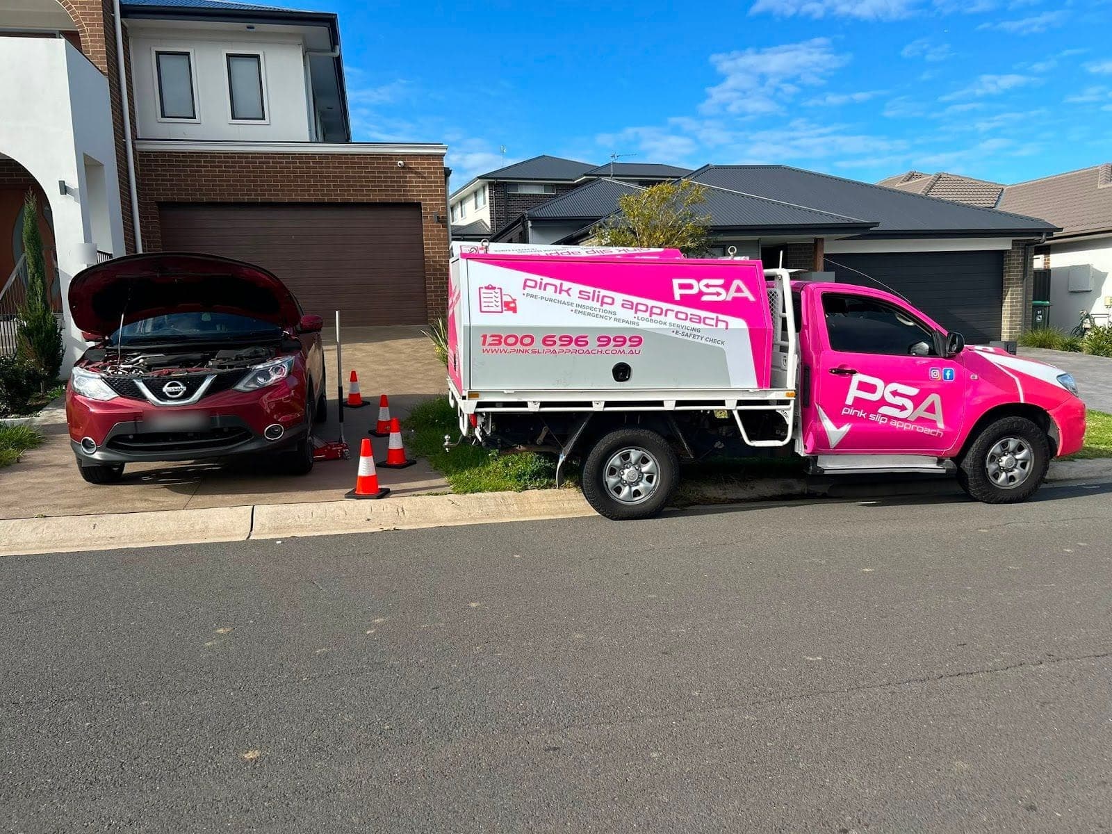 A red Nissan SUV with its bonnet up on a home driveway, cones in front and a pink PSA ute parked at the kerb