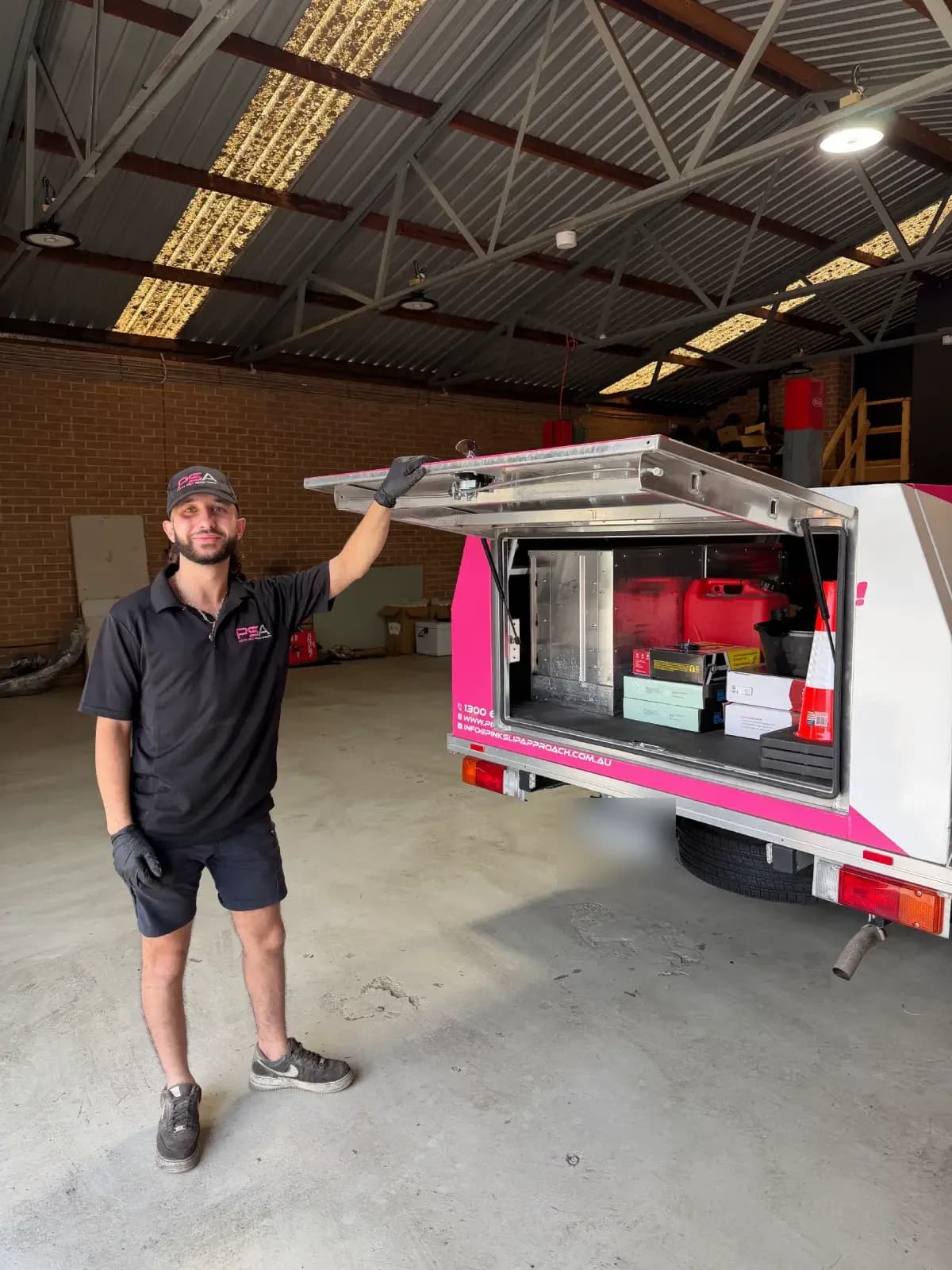 A PSA technician holding open the canopy of a pink PSA service ute, stocked with parts